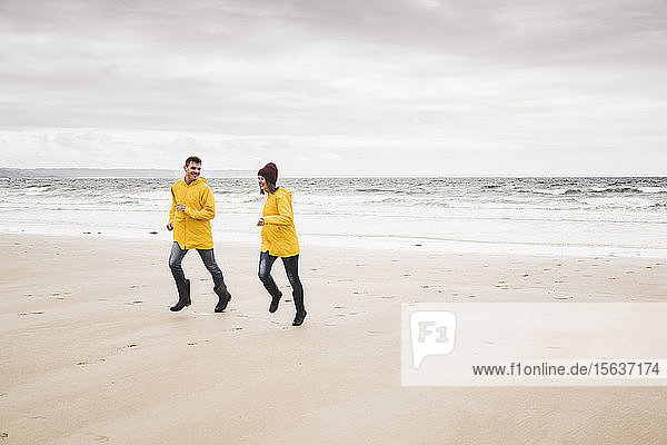 Young woman wearing yellow rain jackets and running at the beach  Bretagne  France