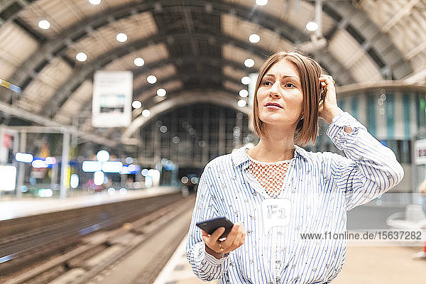 Junge unglückliche Frau benutzt Smartphone am Bahnhof