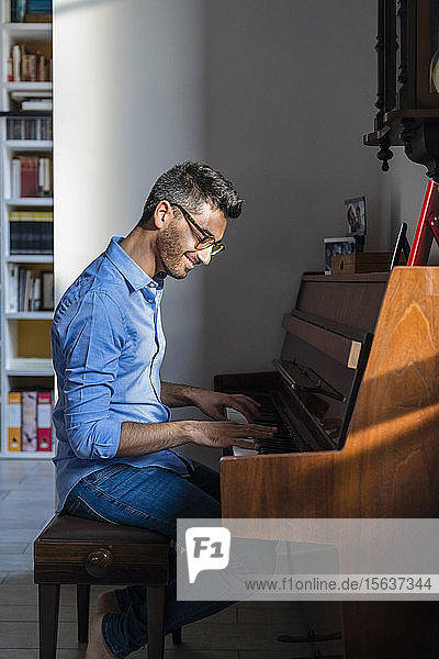 Porträt eines lächelnden jungen Mannes  der zu Hause Klavier spielt
