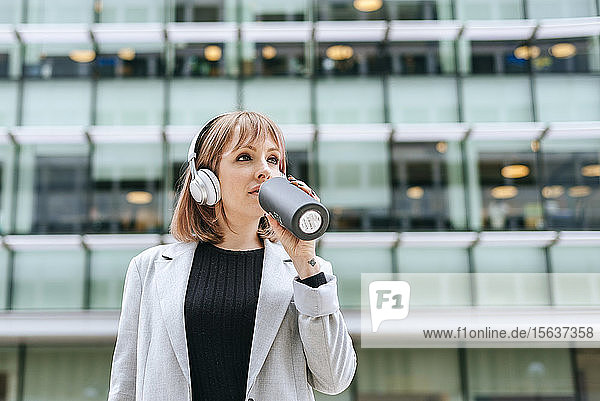 Woman with headphones drinking from reusable bottle in the city