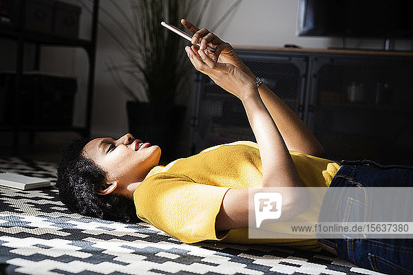 Junge Frau liegt zu Hause auf dem Boden und benutzt ein Smartphone