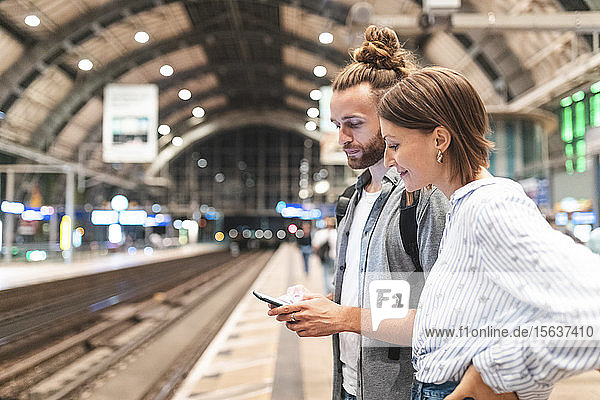 Junges Paar wartet am Bahnhof auf den Zug und benutzt ein Smartphone  Berlin  Deutschland