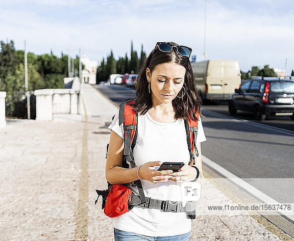 Young female backpacker with red backpack using smartphone in the city  Verona  Italy