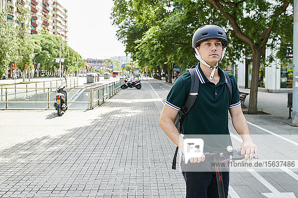 Lässiger junger Geschäftsmann auf dem E-Scooter auf dem Radweg in der Stadt