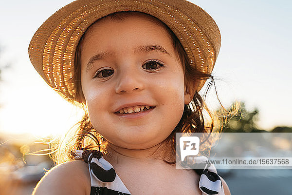 Porträt eines lächelnden kleinen Mädchens mit Strohhut bei Sonnenuntergang