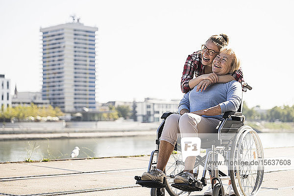 Junge Frau Kopf an Kopf mit ihrer lachenden Großmutter im Rollstuhl sitzend