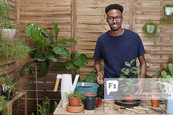 Porträt eines lächelnden jungen Mannes beim Umtopfen einer Pflanze auf seiner Terrasse