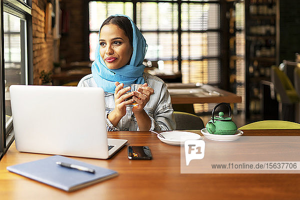 Geschäftsfrau mit türkisfarbenem Hidschab in einem Café  die arbeitet und Tee einschenkt