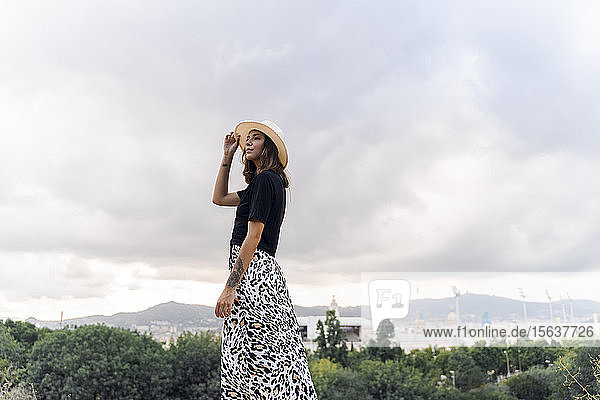 Modische junge Frau mit Sommerhut schaut in die Ferne  Barcelona  Spanien