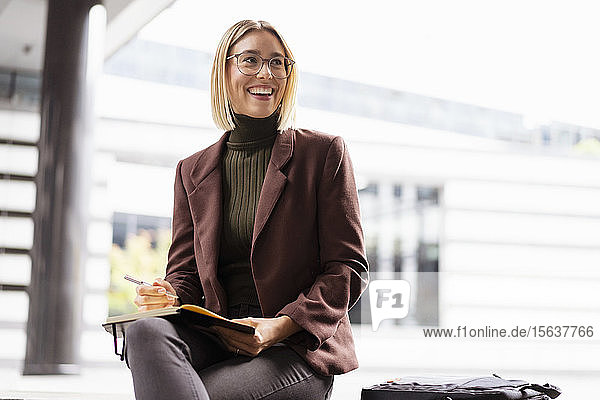 Lächelnde junge Geschäftsfrau mit Notizbuch in der Stadt