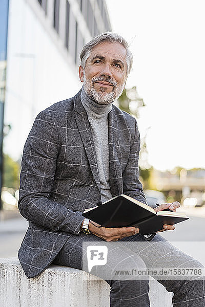 Fashionable mature businessman in the city sitting down with notebook