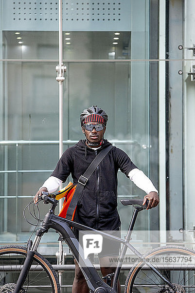 Porträt eines stilvollen jungen Mannes mit Fahrrad und Kuriertasche in der Stadt