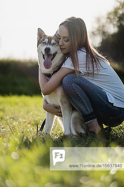 Junge Frau umarmt ihren Hund auf einer Wiese