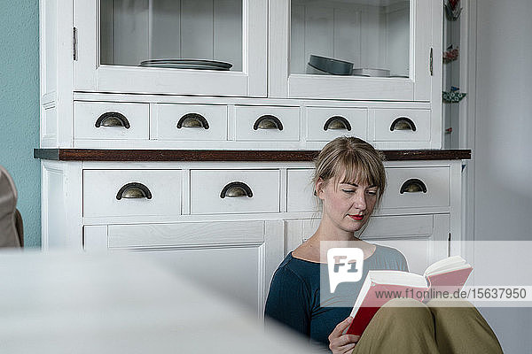 Porträt einer Frau  die in der Küche sitzt und einen Roman liest