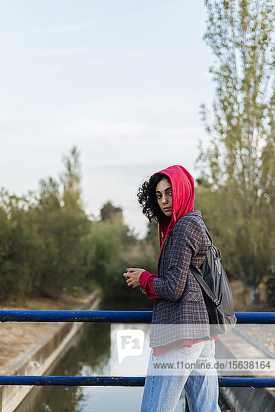 Porträt einer jungen Frau mit Rucksack und Mobiltelefon auf einer Brücke stehend