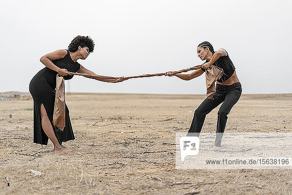 Zwei Frauen ziehen ein Tuch in trostloser Landschaft