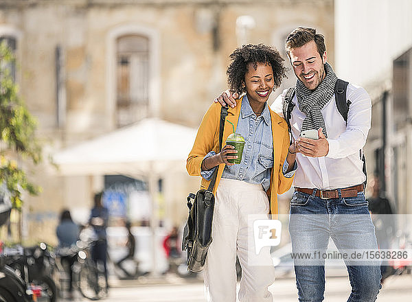 Happy young couple looking at smartphone in the city