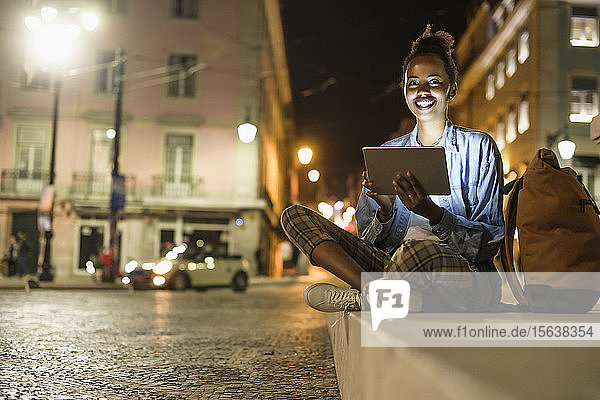 Porträt einer glücklichen jungen Frau mit digitalem Tablet in der Stadt bei Nacht  Lissabon  Portugal