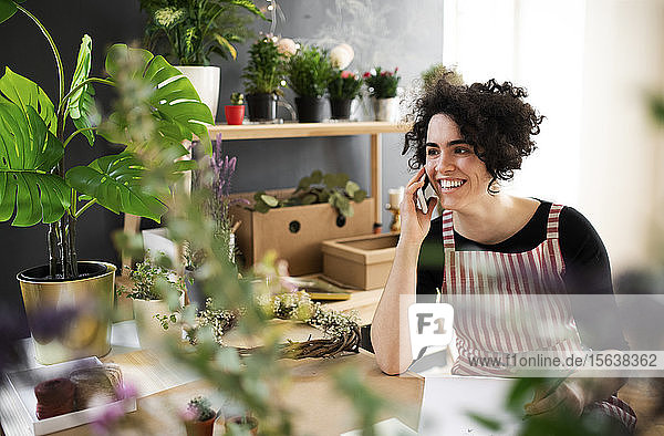 Glückliche junge Frau am Telefon in einem kleinen Laden mit Pflanzen