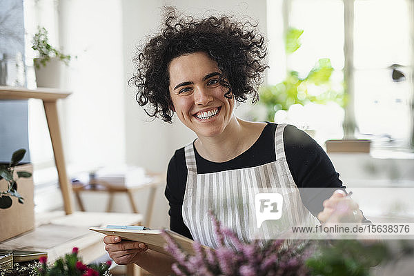 Porträt einer glücklichen jungen Frau mit Klemmbrett in einem kleinen Laden mit Pflanzen