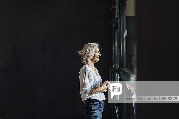 Lässige reife Geschäftsfrau  die im Loft-Büro aus dem Fenster schaut