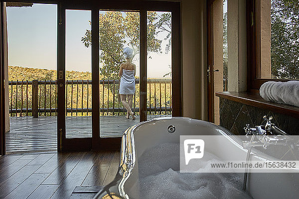 Badewanne voller Schaum und in ein Handtuch gewickelte Frau auf einer Terrasse
