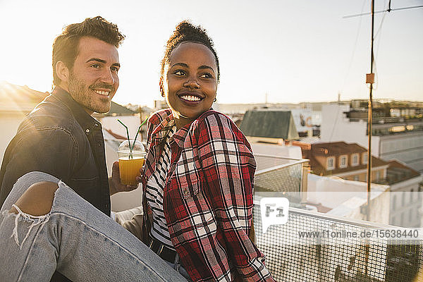 Happy young couple having a drink on rooftop in the evening