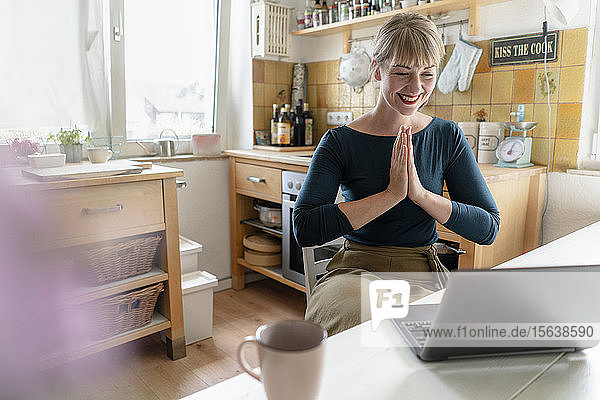 Porträt einer lachenden Frau mit Laptop  die in der Küche Yoga praktiziert