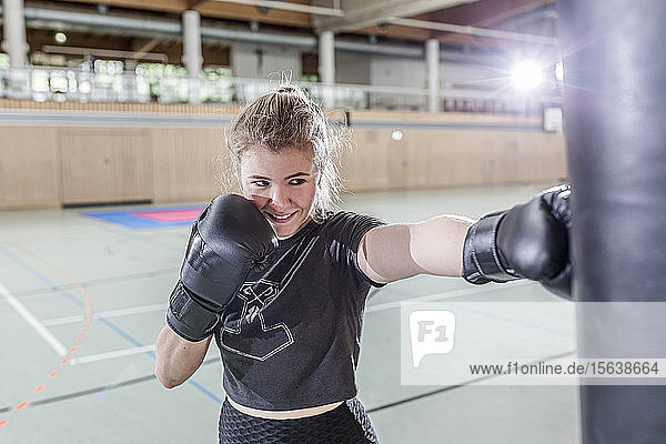 Smiling female boxer practising at punchbag in sports hall