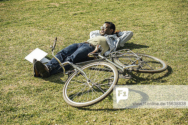 Junger Mann mit Fahrrad  entspannend  im Gras liegend