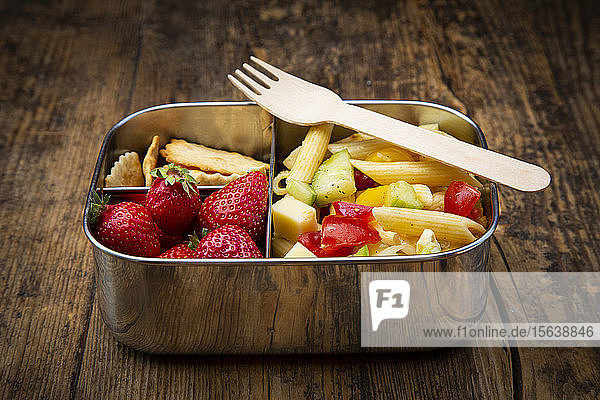 Nahaufnahme von Nudeln mit Erdbeeren und Crackern in Lunchbox auf Holztisch