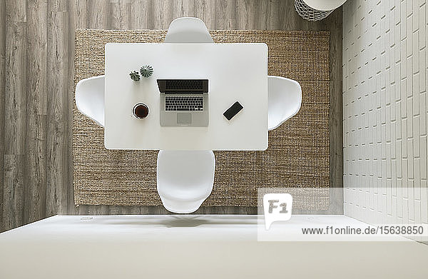 White table with laptop smartphone and cup of coffee at modern loft seen from above