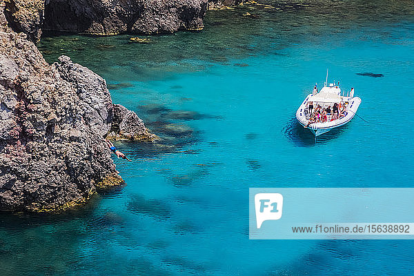 Tourists on a tour boat at Tsigado Beach with a young man diving off a cliff; Milos Island Cyclades Greece