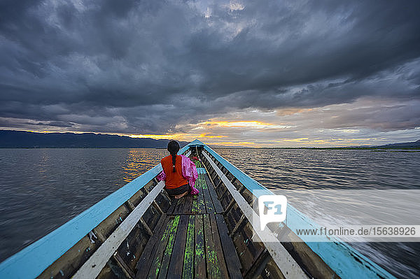 A Burmese woman sits in a wooden long boat on Inle Lake at sunset; Yawngshwe  Shan State  Myanmar