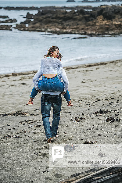 Ein junges Paar am Strand  die junge Frau wird auf dem Rücken des jungen Mannes getragen; Wellington  Nordinsel  Neuseeland