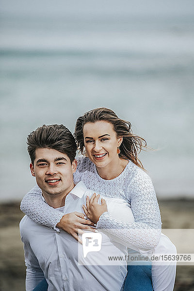 Porträt eines jungen Paares am Strand  die junge Frau wird auf dem Rücken des jungen Mannes getragen; Wellington  Nordinsel  Neuseeland