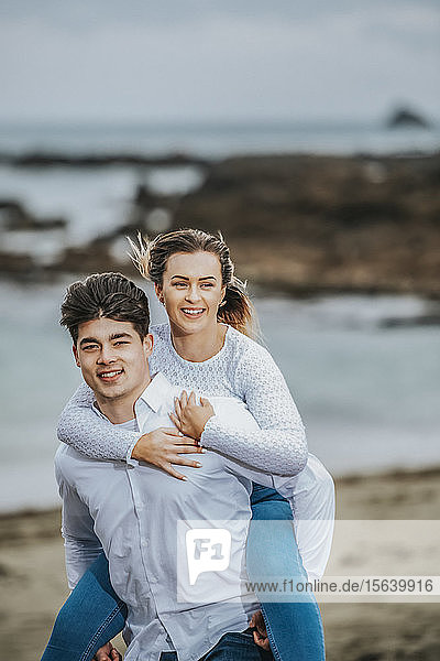 Portrait of a young couple at the beach  the young woman being carried on the young man's back; Wellington  North Island  New Zealand