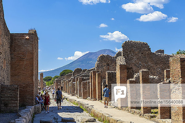Tourists walk through the excavated ruins down a street in Pompeii with Mount Vesuvius in the background; Pompeii  Province of Naples  Campania  Italy