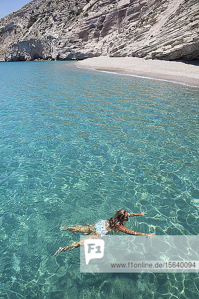 Female tourist swimming in the clear  turquoise water of Galazia Nera Bay; Polyaigos Island  Cyclades  Greece