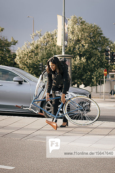 Businesswoman holding bicycle while crossing street in city