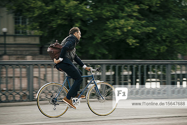 Seitenansicht eines Geschäftsmannes mit Tasche beim Fahrradfahren auf der Brücke