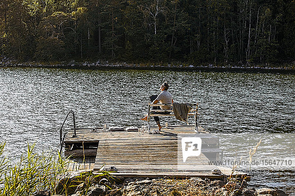 Nachdenklicher Mann mit Laptop sitzt auf Bank über Steg am See