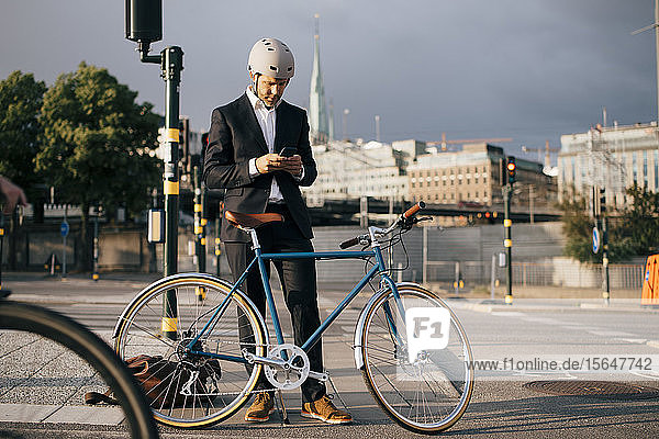 Geschäftsmann benutzt Mobiltelefon  während er mit dem Fahrrad auf der Straße in der Stadt steht