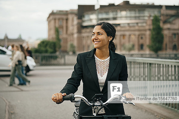 Lächelnde Geschäftsfrau mit Fahrrad auf einer Brücke in der Stadt