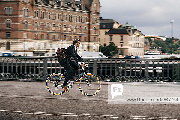 Seitenansicht eines Geschäftsmannes  der auf der Straße in der Stadt Fahrrad fährt