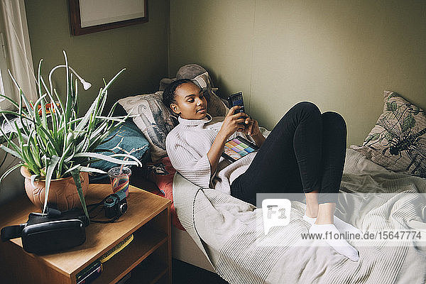 Weiblicher Teenager benutzt Mobiltelefon  während er zu Hause im Bett liegt