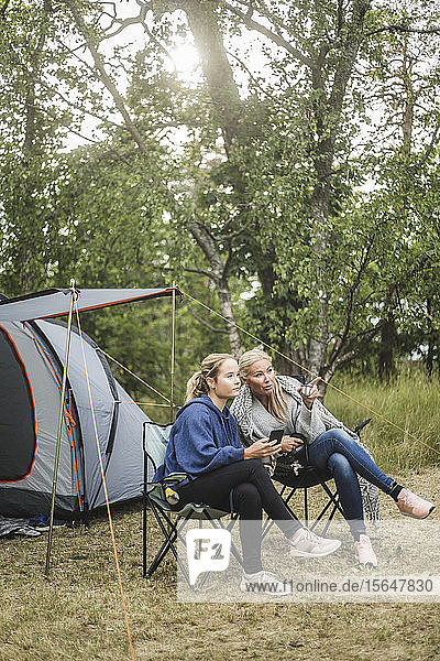 Frau in voller Länge im Gespräch mit der Tochter  während sie auf dem Campingplatz sitzt
