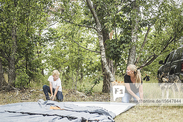 Smiling mother and son pitching tent in forest