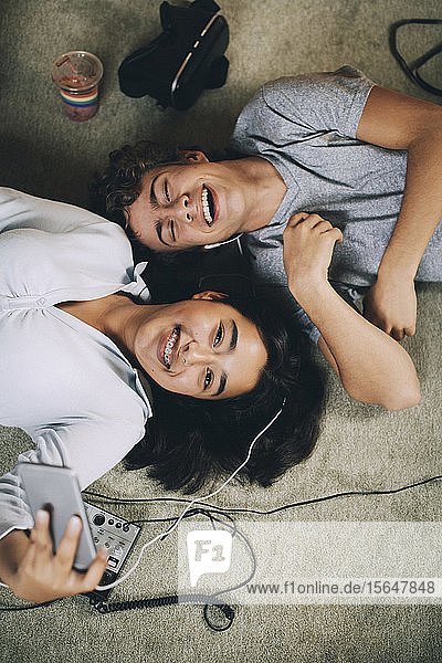Directly above shot of happy friends listening music together while lying on carpet at home