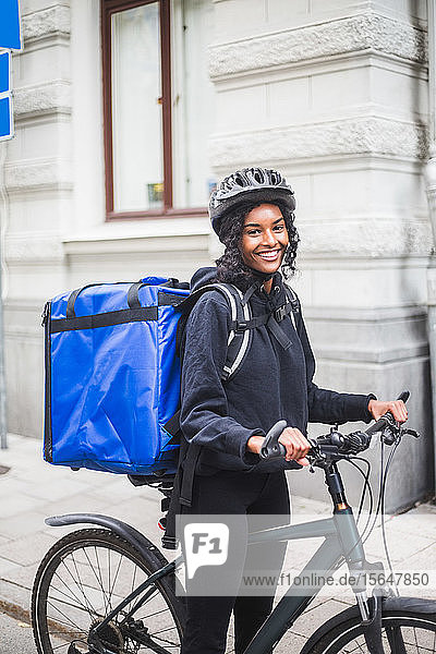 Portrait of smiling delivery woman with bicycle in city